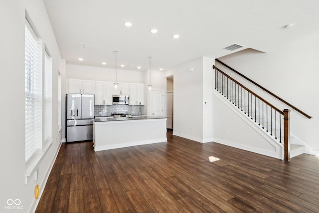 kitchen featuring visible vents, hanging light fixtures, fridge with ice dispenser, stainless steel microwave, and an island with sink