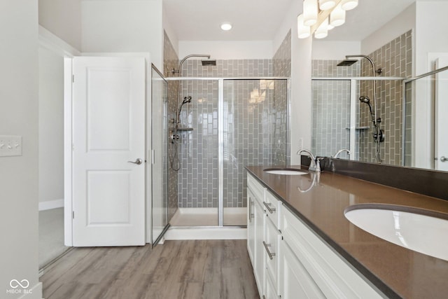 bathroom featuring double vanity, wood finished floors, a stall shower, and a sink