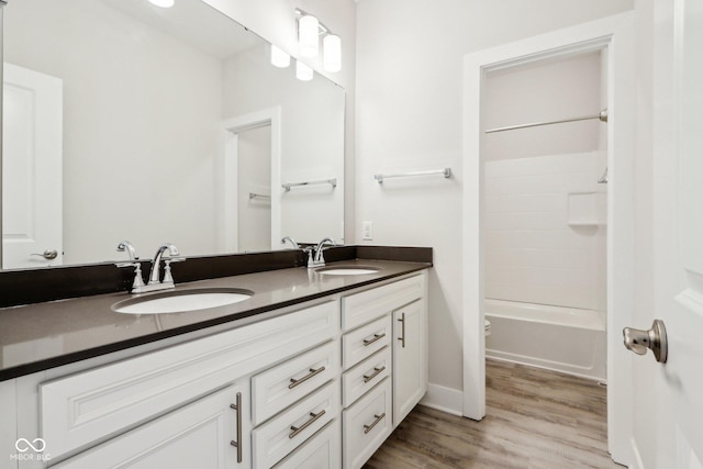 bathroom featuring double vanity, shower / washtub combination, a sink, and wood finished floors