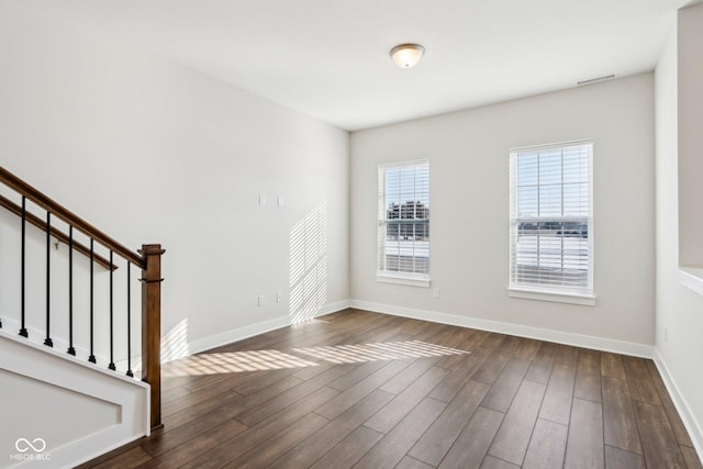 unfurnished room with stairs, dark wood-style flooring, visible vents, and baseboards