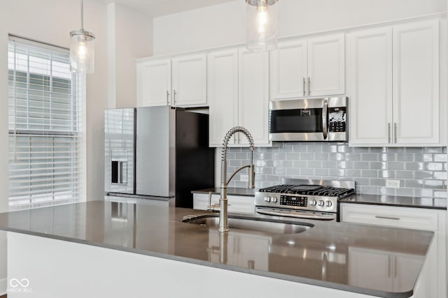 kitchen featuring decorative backsplash, dark countertops, appliances with stainless steel finishes, hanging light fixtures, and white cabinetry