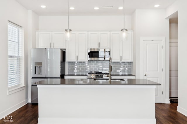 kitchen featuring stainless steel microwave, a kitchen island with sink, and pendant lighting