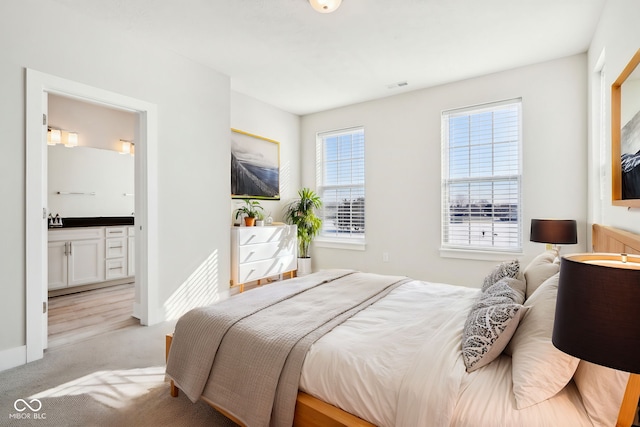 bedroom featuring light carpet, ensuite bath, visible vents, and baseboards