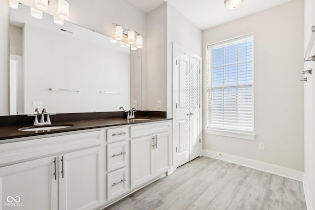 full bathroom featuring double vanity, baseboards, a sink, and wood finished floors