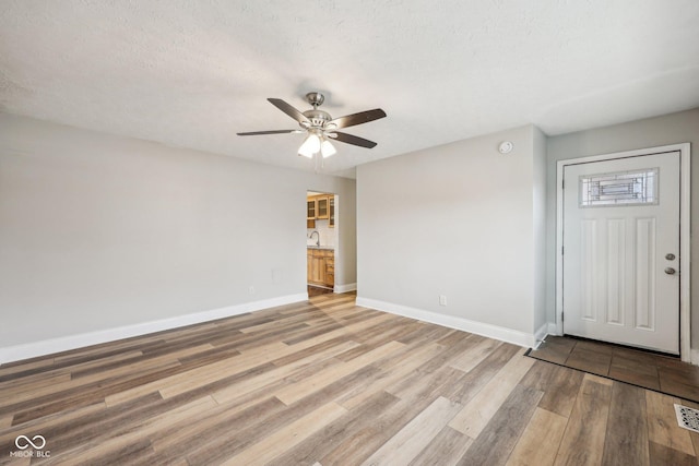 empty room with sink, light hardwood / wood-style floors, a textured ceiling, and ceiling fan