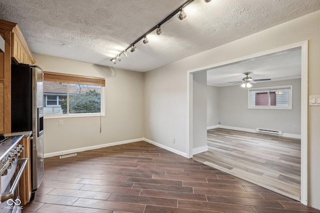 interior space with rail lighting, ceiling fan, appliances with stainless steel finishes, a baseboard heating unit, and a textured ceiling