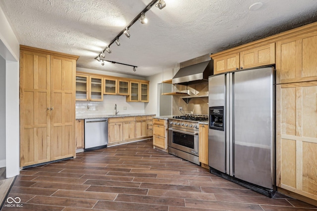 kitchen featuring wall chimney range hood, sink, appliances with stainless steel finishes, light stone counters, and tasteful backsplash