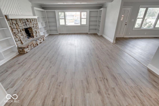 1002 Payton Ave, Indianapolis, IN 46219 - unfurnished living room featuring built in shelves, a stone fireplace, and light hardwood / wood-style floors