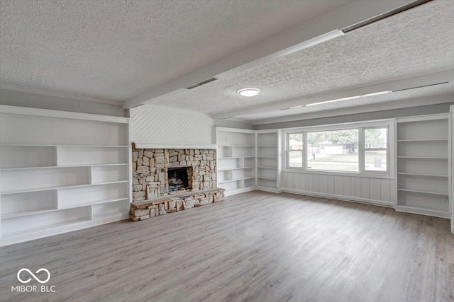 unfurnished living room featuring beam ceiling, hardwood / wood-style flooring, a stone fireplace, and a textured ceiling