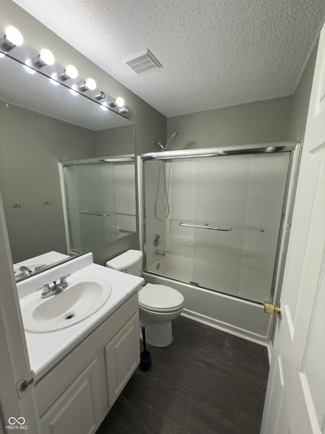 full bathroom with hardwood / wood-style flooring, shower / bath combination with glass door, vanity, a textured ceiling, and toilet