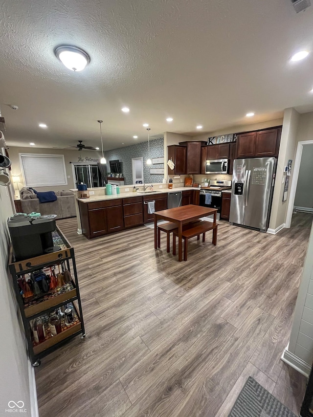 kitchen featuring appliances with stainless steel finishes, decorative light fixtures, a center island, dark brown cabinetry, and light hardwood / wood-style flooring