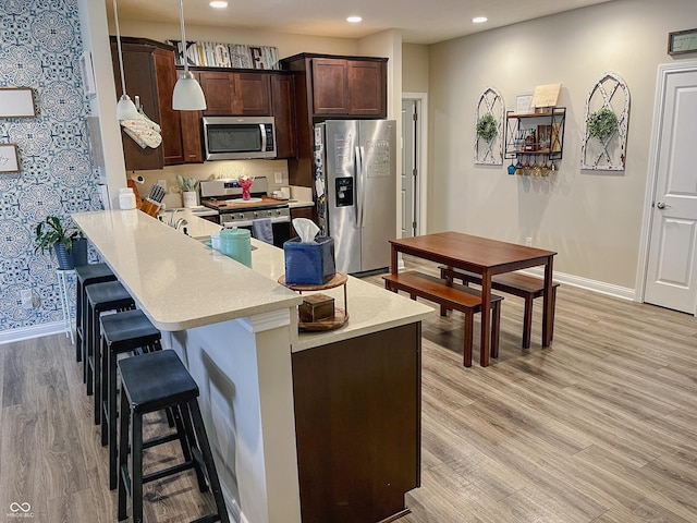 kitchen with decorative light fixtures, a kitchen breakfast bar, kitchen peninsula, stainless steel appliances, and light hardwood / wood-style flooring