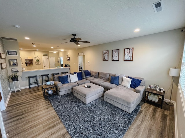 living room featuring a textured ceiling, recessed lighting, wood finished floors, visible vents, and baseboards