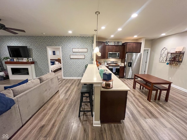 kitchen featuring a kitchen bar, hanging light fixtures, dark brown cabinetry, stainless steel appliances, and light wood-type flooring