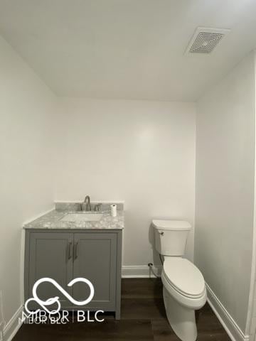 half bathroom featuring toilet, vanity, visible vents, and baseboards