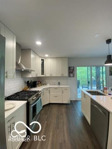 kitchen with dark wood-style flooring, stainless steel appliances, white cabinets, a sink, and wall chimney exhaust hood