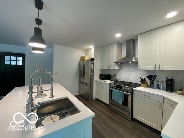 kitchen with dark wood finished floors, light countertops, appliances with stainless steel finishes, a sink, and wall chimney exhaust hood