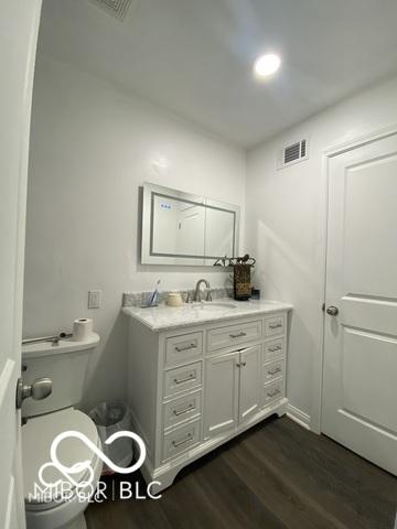 half bathroom with toilet, vanity, wood finished floors, and visible vents