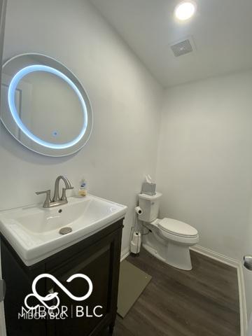 half bath featuring visible vents, toilet, vanity, wood finished floors, and baseboards