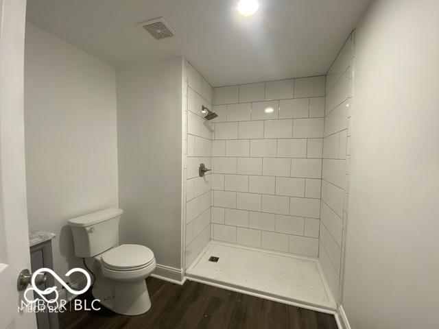 full bath featuring baseboards, visible vents, tiled shower, toilet, and wood finished floors