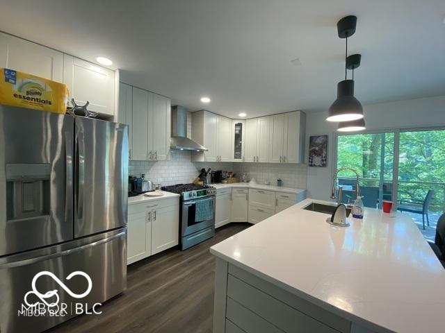 kitchen with appliances with stainless steel finishes, backsplash, wall chimney range hood, and white cabinetry