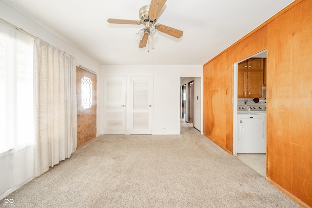 spare room with light carpet, independent washer and dryer, ceiling fan, and wood walls