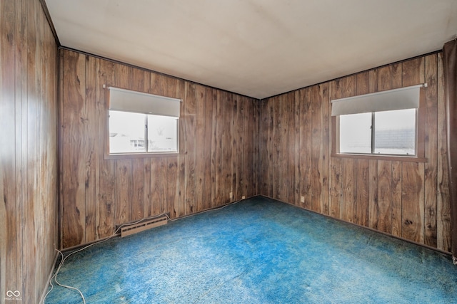 spare room with wood walls, baseboard heating, and dark colored carpet