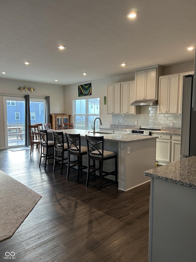 kitchen featuring stainless steel refrigerator, a center island with sink, light stone counters, a kitchen bar, and dark hardwood / wood-style flooring