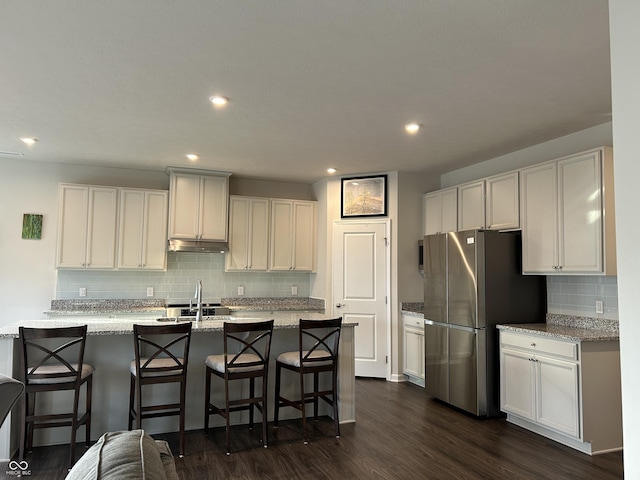 kitchen with light stone counters, stainless steel fridge, a breakfast bar area, and white cabinets