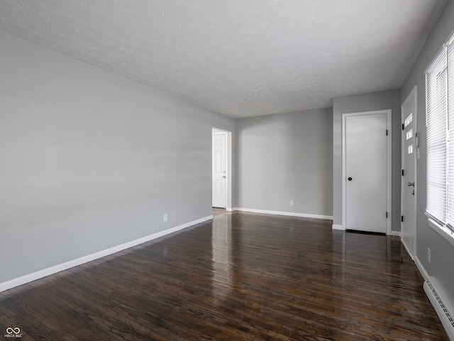 spare room with a baseboard heating unit, a textured ceiling, and dark hardwood / wood-style floors