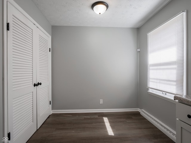 unfurnished bedroom with a baseboard heating unit, dark wood-type flooring, a closet, and a textured ceiling