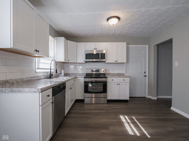 kitchen featuring appliances with stainless steel finishes, sink, white cabinets, dark hardwood / wood-style flooring, and decorative backsplash