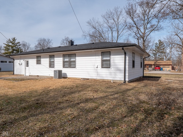 rear view of property featuring central air condition unit and a lawn