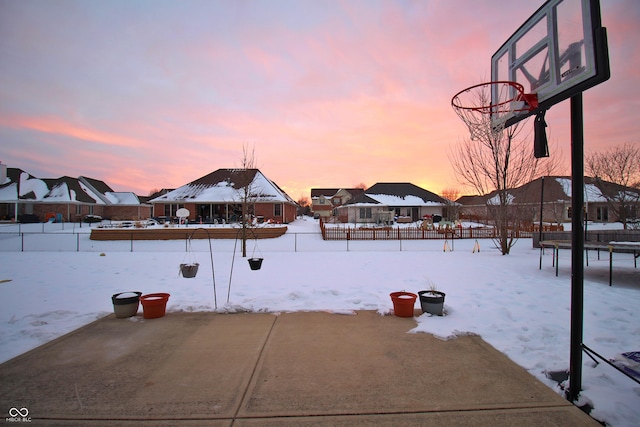 yard covered in snow with basketball court and a trampoline