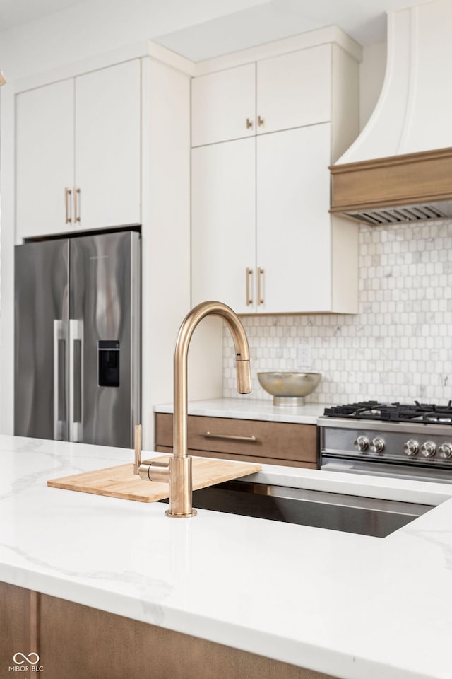 kitchen with premium range hood, white cabinetry, stainless steel appliances, tasteful backsplash, and light stone countertops