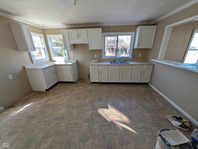 kitchen featuring a sink, baseboards, white cabinets, light countertops, and crown molding