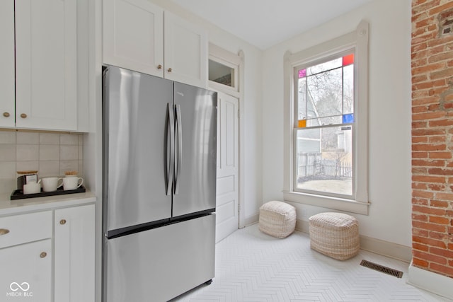 kitchen featuring white cabinets, tasteful backsplash, brick wall, and stainless steel fridge