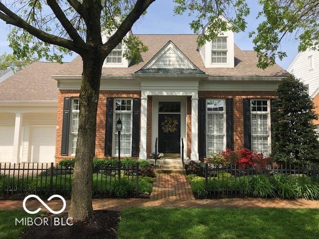 new england style home featuring a garage, brick siding, and a fenced front yard