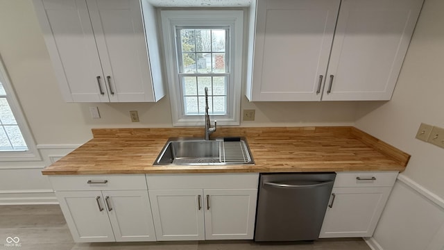 kitchen featuring butcher block counters, sink, stainless steel dishwasher, and white cabinets