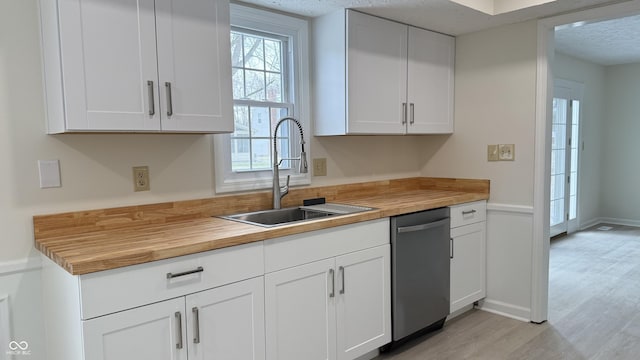 kitchen with sink, light wood-type flooring, white cabinets, stainless steel dishwasher, and a textured ceiling