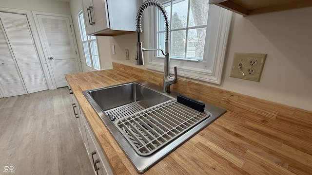 interior space featuring white cabinets, sink, wooden counters, and light hardwood / wood-style floors