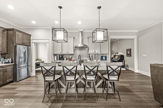 kitchen with stainless steel fridge, a breakfast bar, a kitchen island with sink, and wall chimney range hood