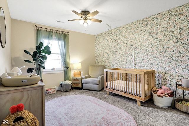 bedroom with a crib, ceiling fan, and carpet flooring