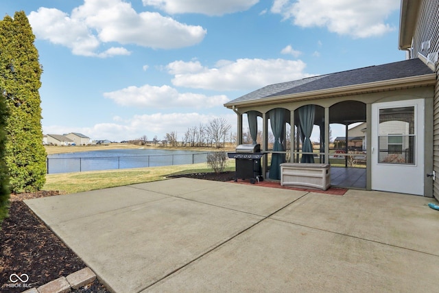 view of patio featuring area for grilling, fence, and a water view