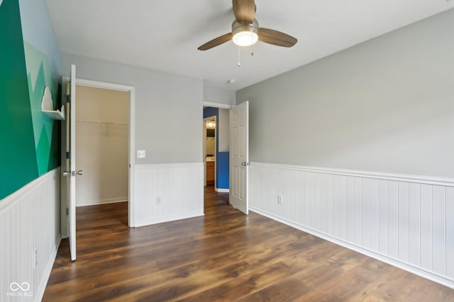 unfurnished bedroom with a wainscoted wall, wood finished floors, and a spacious closet