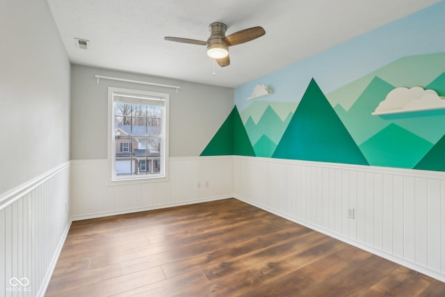 unfurnished room with a ceiling fan, visible vents, wood finished floors, a wainscoted wall, and lofted ceiling