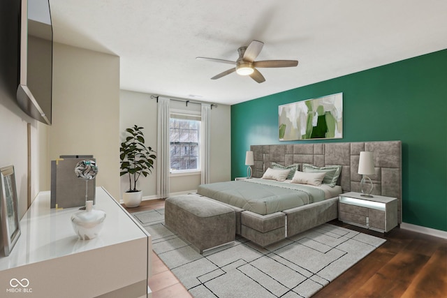 bedroom with ceiling fan, an accent wall, baseboards, and wood finished floors