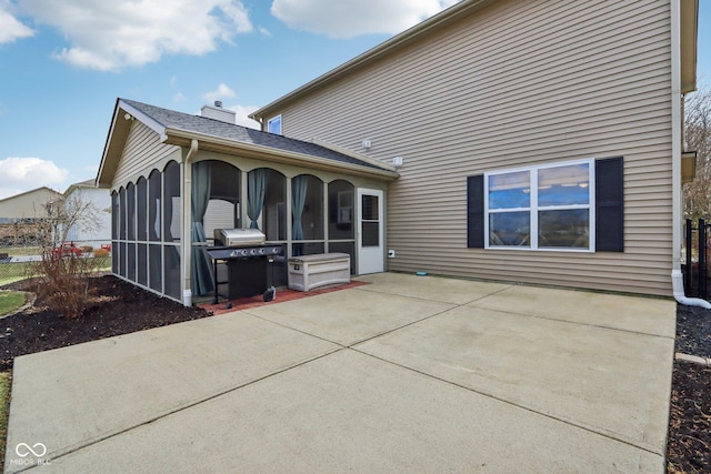 rear view of house featuring a chimney, roof with shingles, a patio, and a sunroom