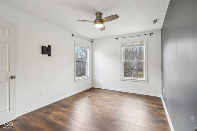 spare room featuring baseboards, plenty of natural light, a textured ceiling, and dark wood-style floors