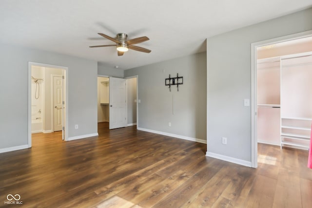 unfurnished bedroom with a spacious closet, ceiling fan, baseboards, a closet, and dark wood-style floors